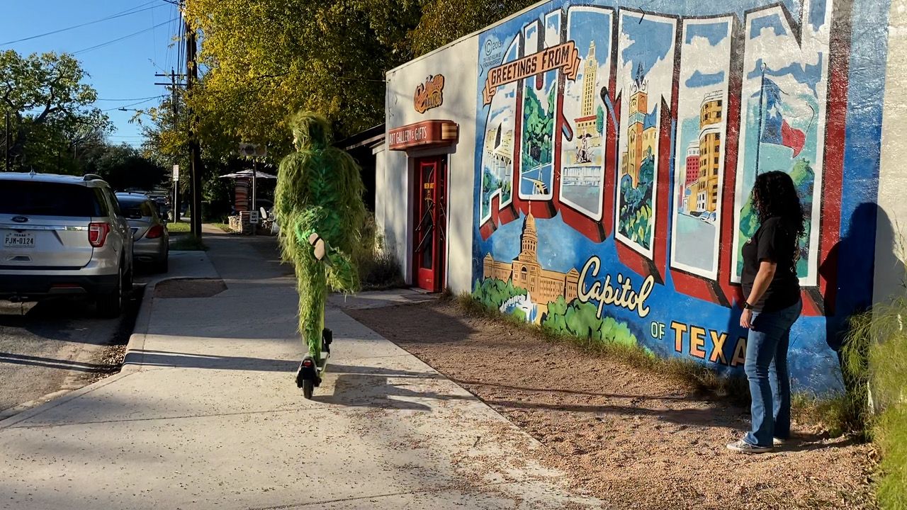 The Grinch riding a scooter in front of an Austin City Mural